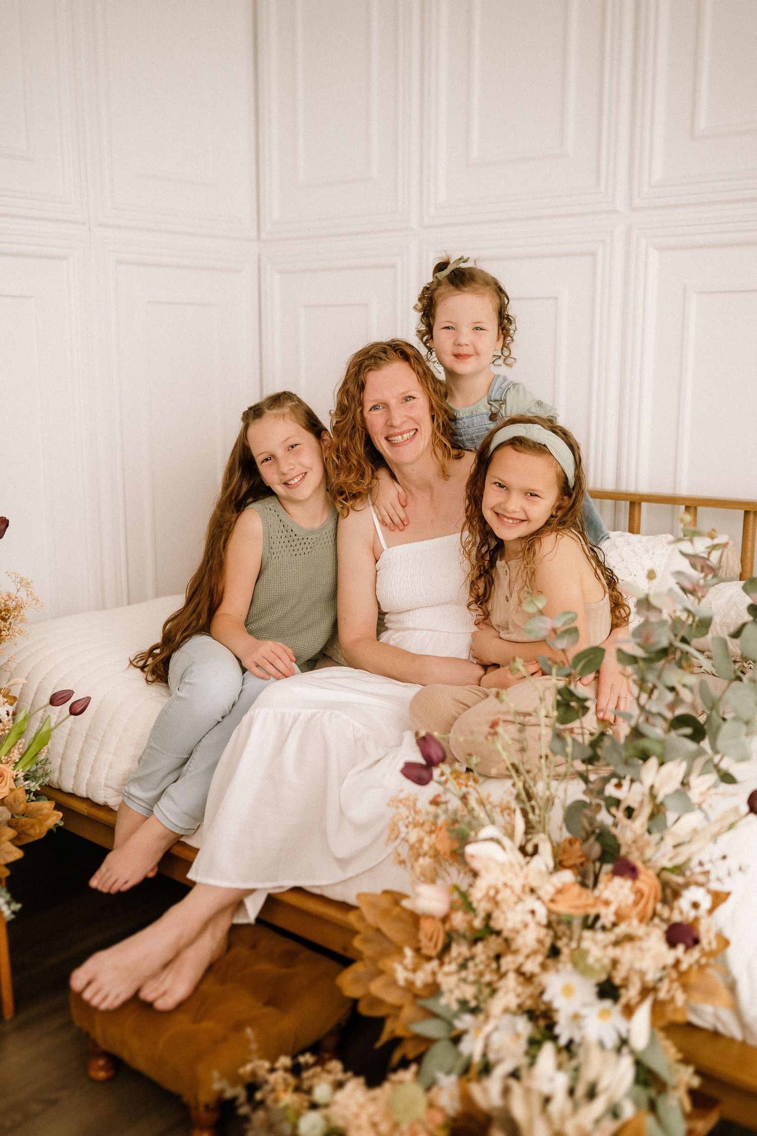 Family portrait in white room with floral arrangements and wooden bench showing tender moments together.