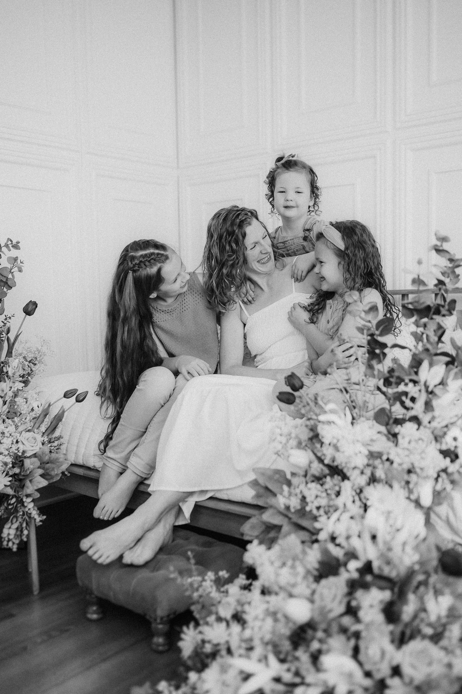 Joyful family moment captured in black and white with floral decorations against white paneled wall.