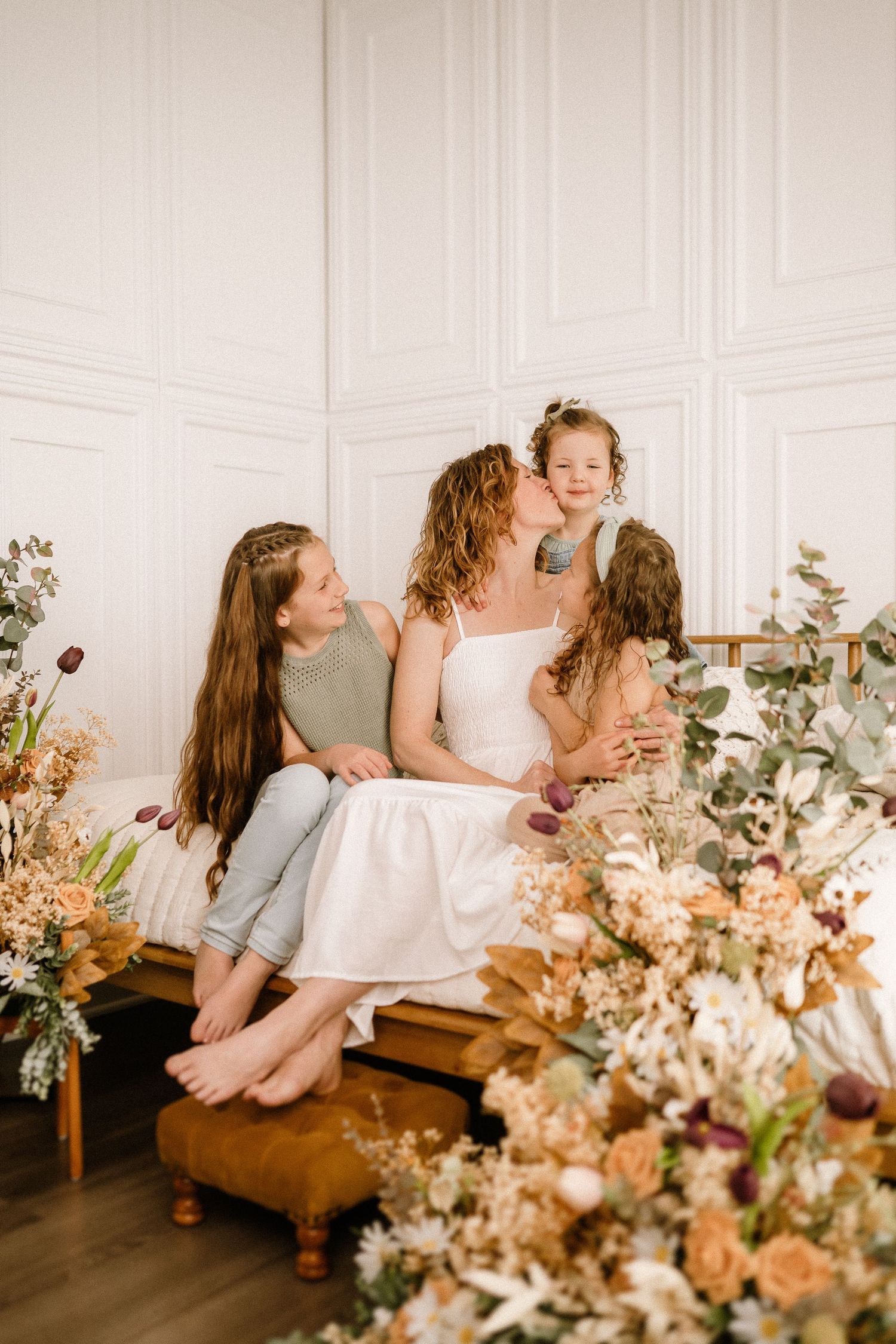 Intimate family portrait in white room with ornate floral arrangements featuring dried flowers and greenery in warm tones.