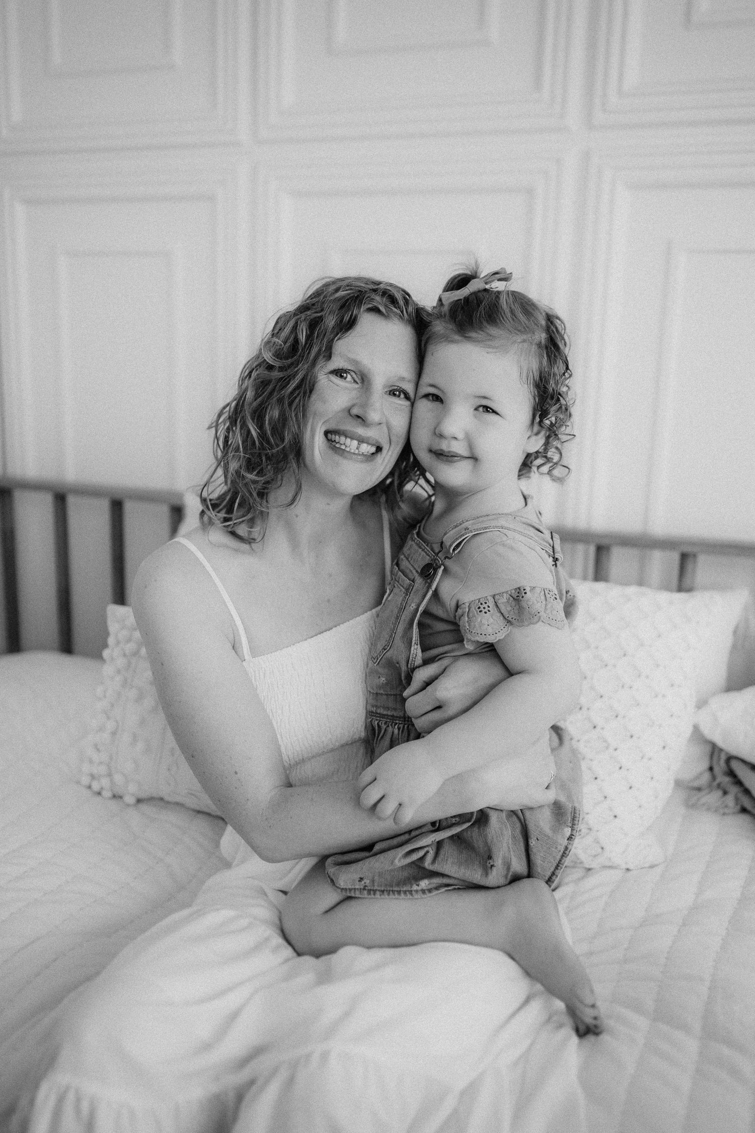 Black and white portrait of a tender moment shared between adult and child on a bed with decorative white wall panels.