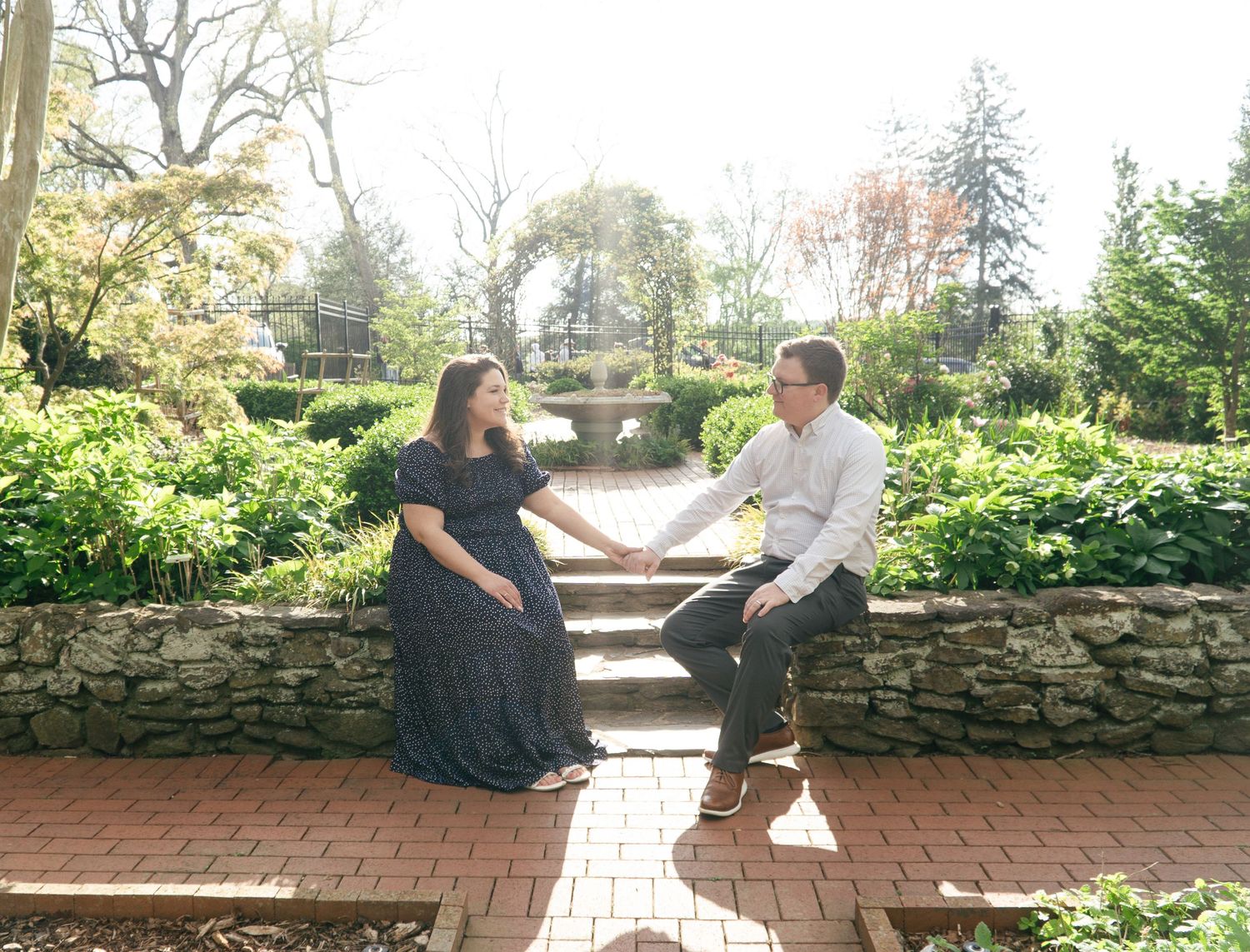 Couple sits on a rustic stone wall bench in a garden setting.