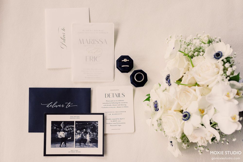A collection of elegant wedding stationery with white flowers and navy accents arranged in a flat lay composition.