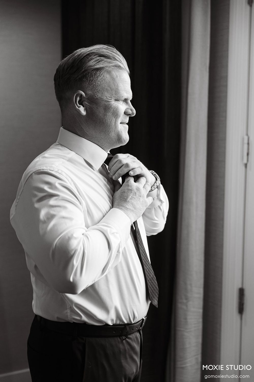 Black and white photo series showing a groom adjusting his tie while getting ready for the wedding ceremony.