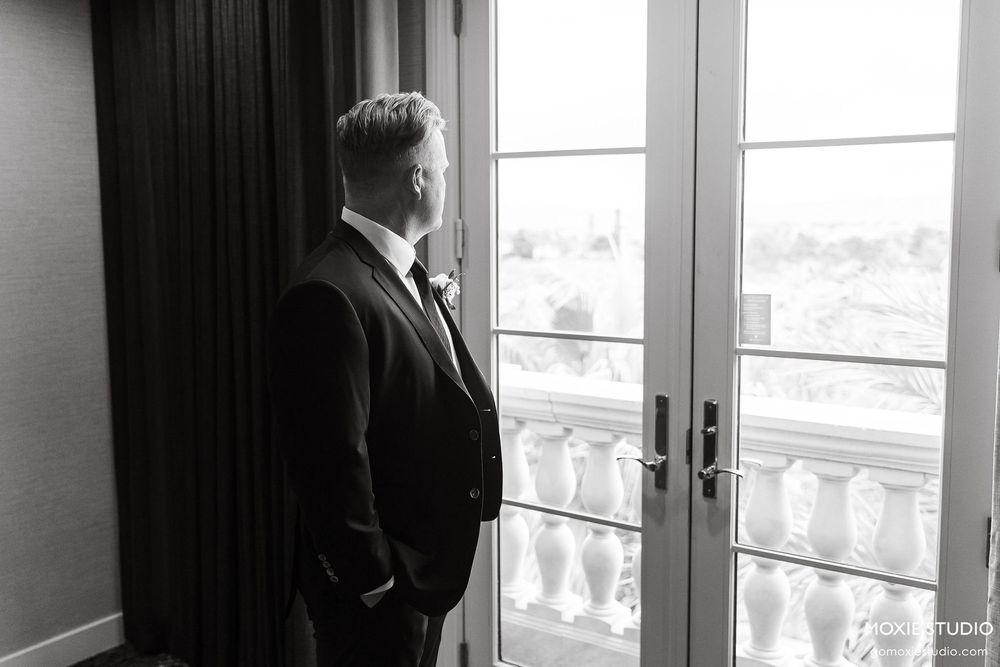 A black and white photograph shows a silhouetted figure standing by bright windows in an elegant room.