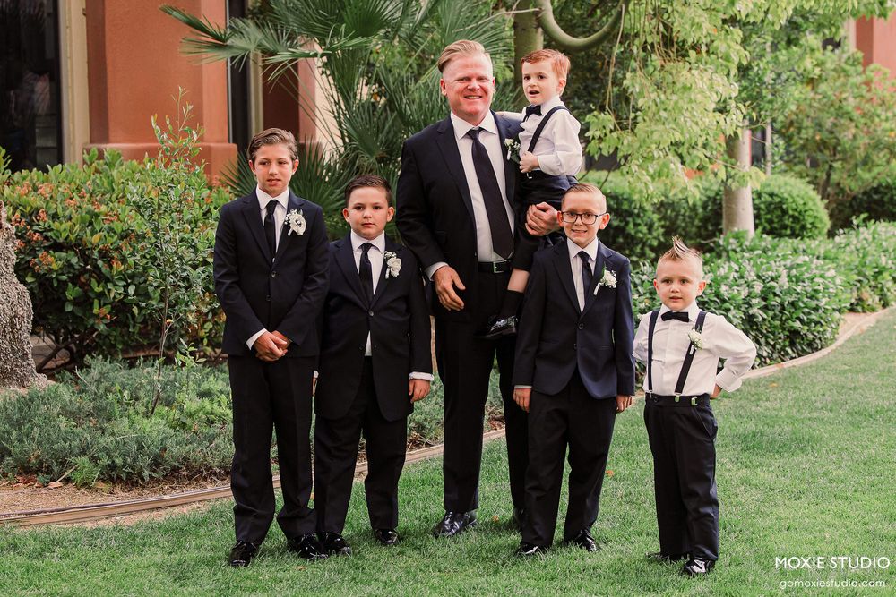 A group in formal attire walks along a garden path during an outdoor wedding celebration.