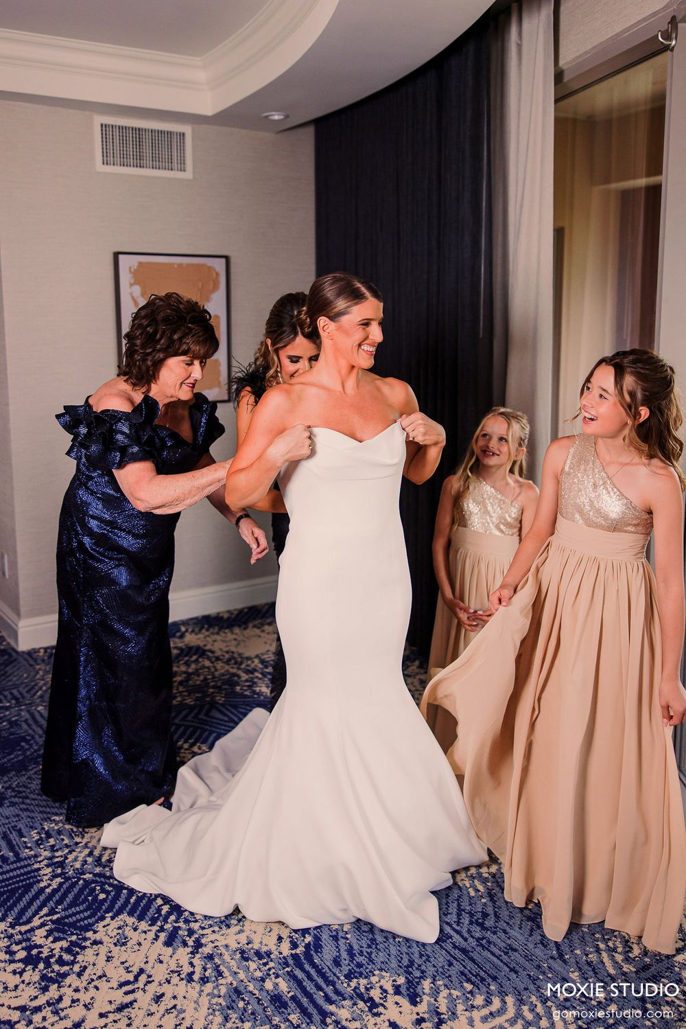 Wedding party having fun with bridesmaids in champagne dresses and navy blue gowns dancing together indoors.