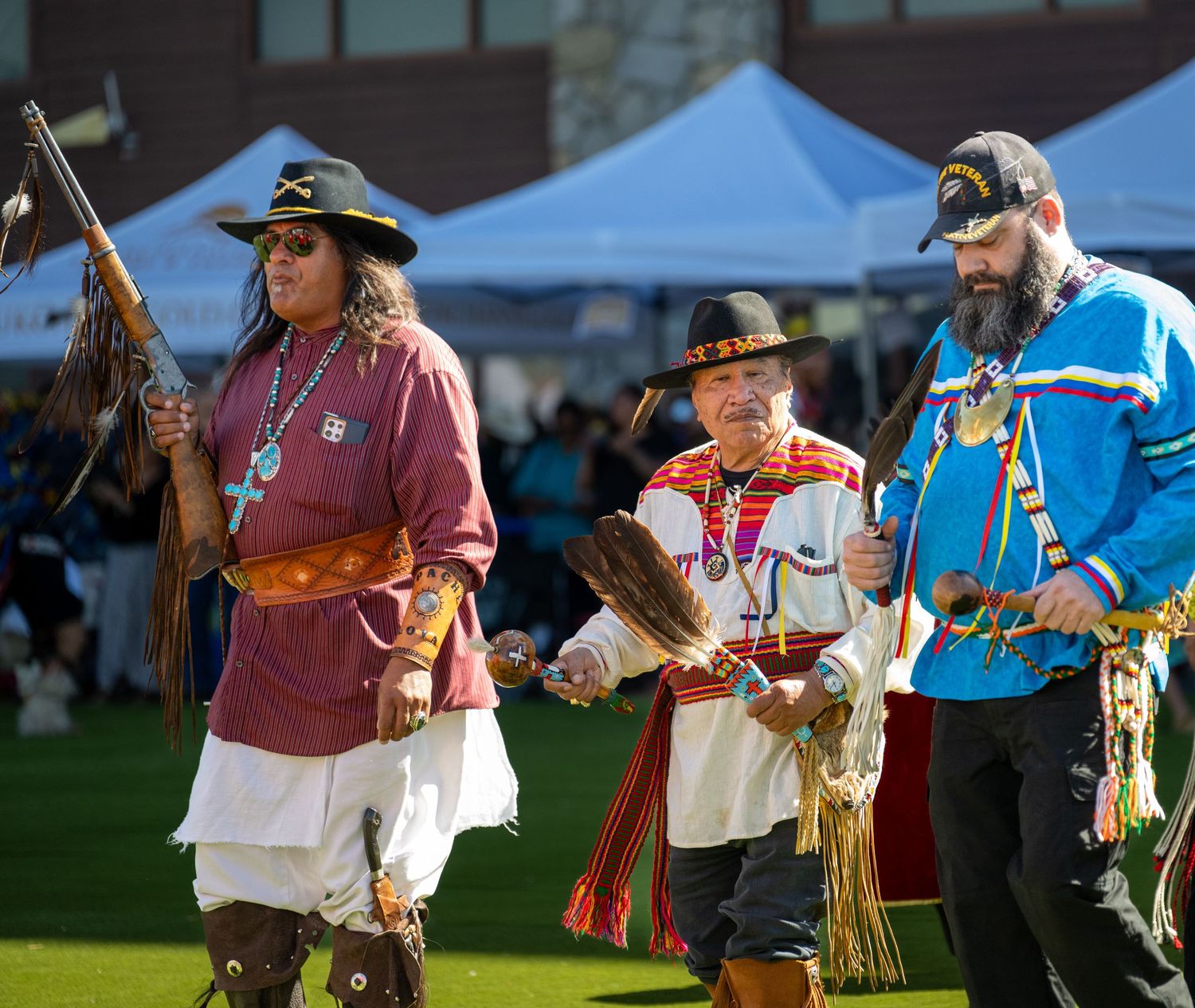 Community members gather outdoors for a cultural celebration under blue tents.