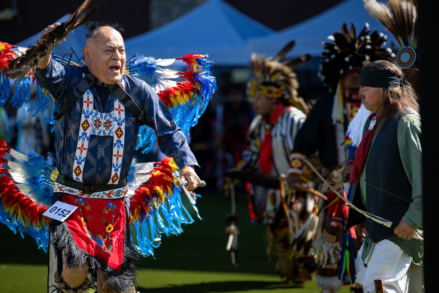 Dancers in feathered regalia perform traditional movements at an outdoor powwow.
