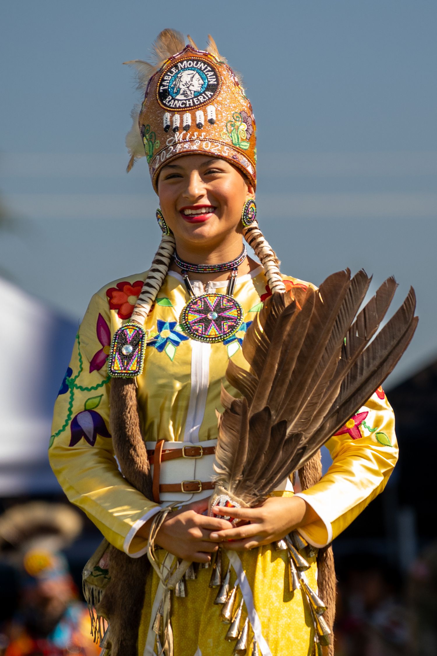A performer in vibrant yellow traditional Native American regalia holds feathers.