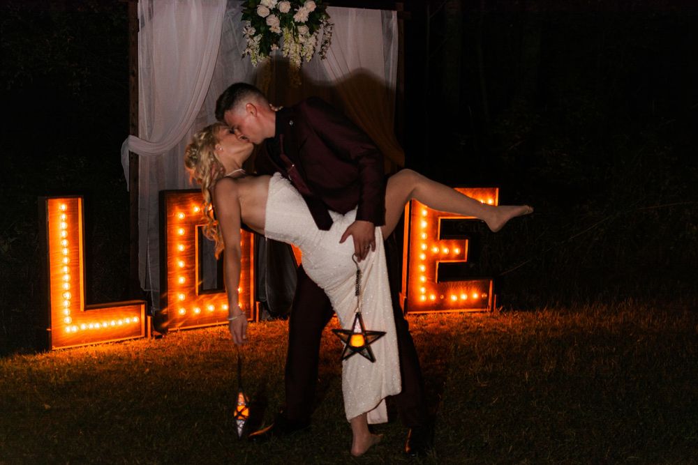 Romantic dancing silhouettes against glowing orange letters at a nighttime wedding celebration.