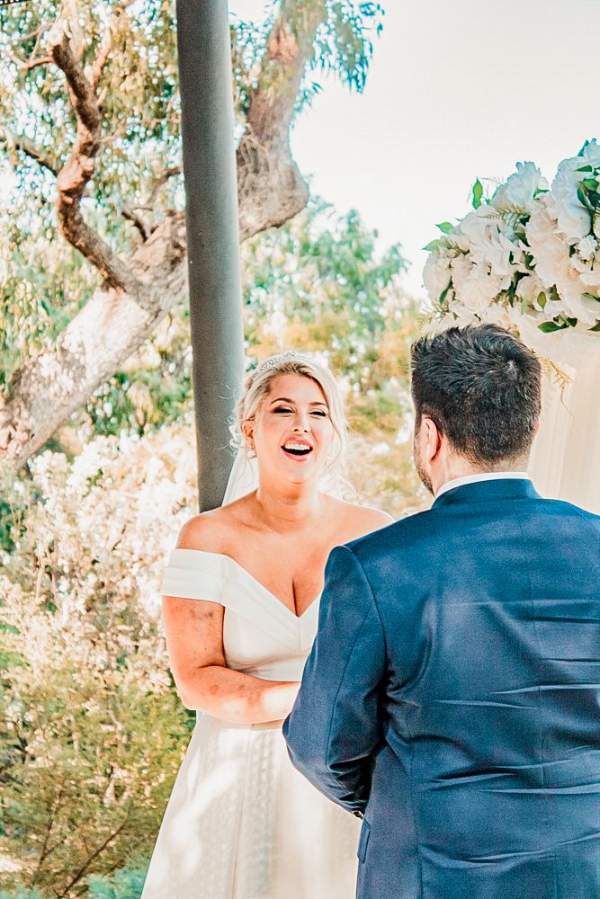 A joyful wedding ceremony moment captured in a sunlit garden setting with white floral decorations.