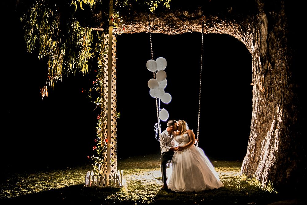 A romantic nighttime swing scene with fairy lights and a couple embracing under a decorated tree.