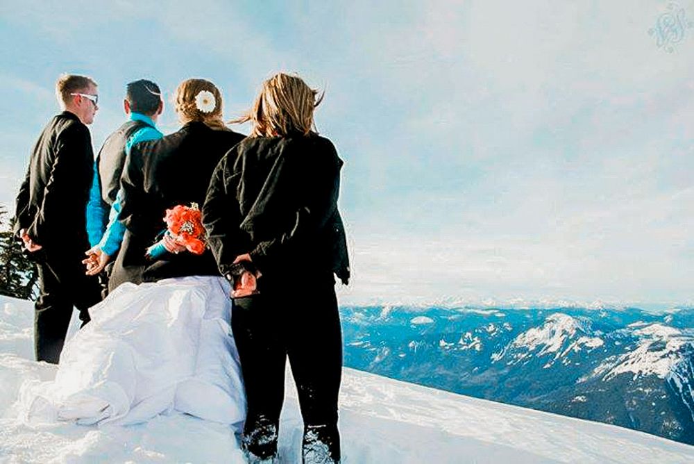 A wedding ceremony takes place on a snowy mountain summit with stunning mountain vistas in the background.
