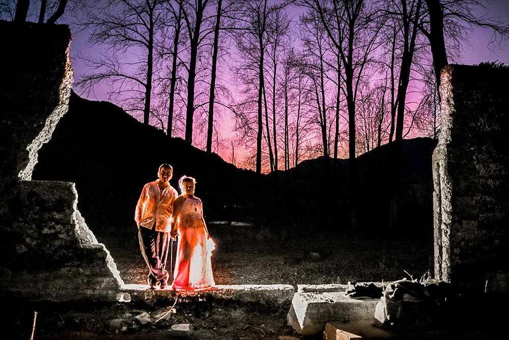 Dramatic wedding portrait with a purple sunset and silhouetted trees through a stone frame.