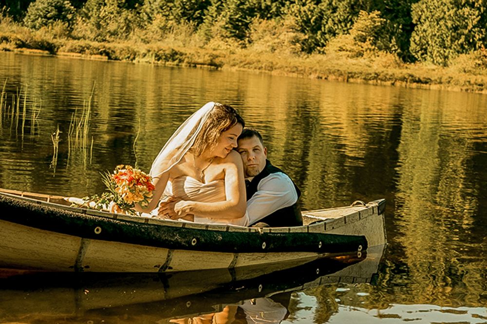 Golden hour wedding photo of couple in wooden canoe on tranquil lake.