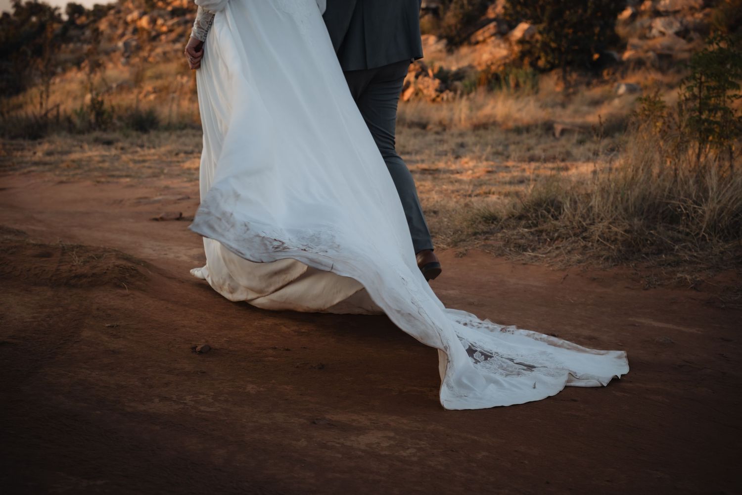 Figure in a white lace dress holds a colorful autumn wedding bouquet with orange and red flowers outdoors.