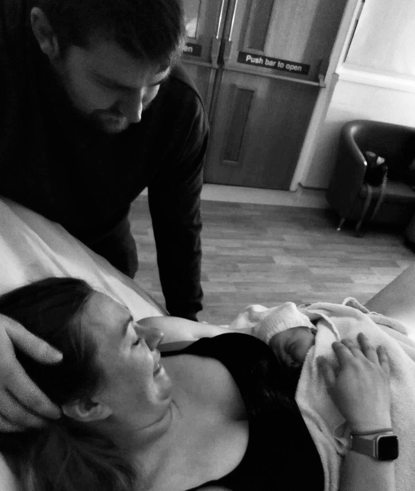 Black and white photo showing a person in labor during childbirth while being supported by their birth partner at bedside.