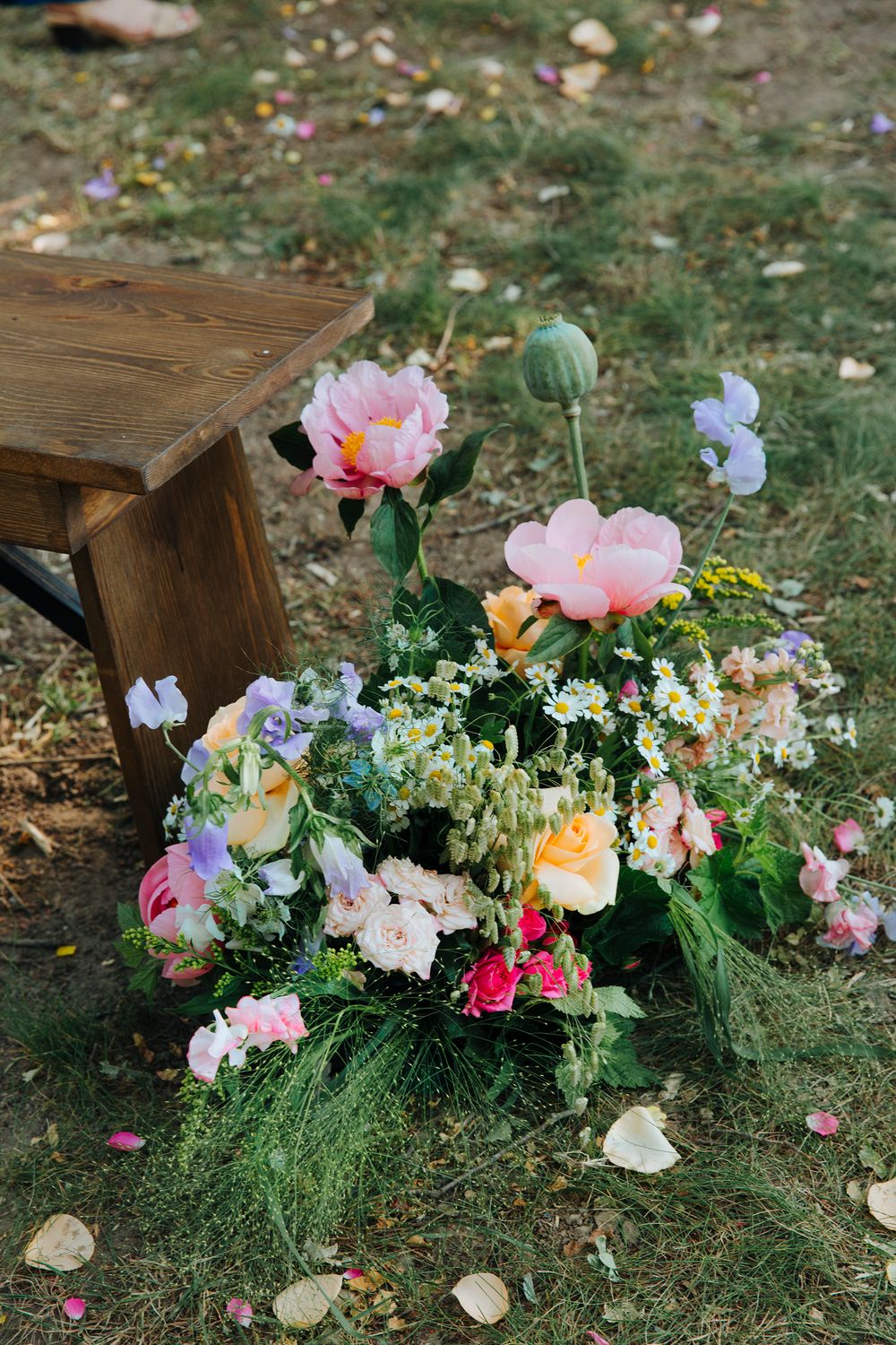 Vibrant floral arrangements with pink and peach blooms decorate wooden benches on grassy ground.