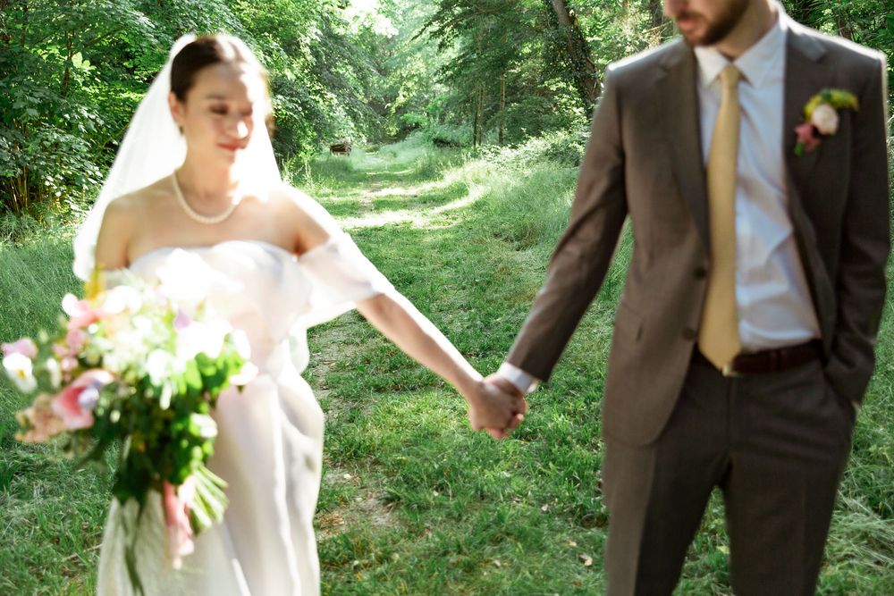 Wedding couple walking through a lush green garden path on a sunny afternoon.