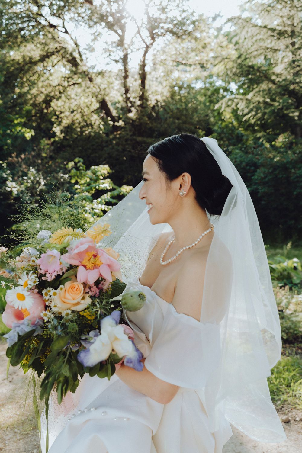 Bride in white dress holding a colorful bouquet of pink and peach flowers in a garden setting.