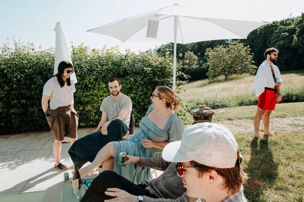 Wedding guests gather outdoors on a sunny day in a garden setting.