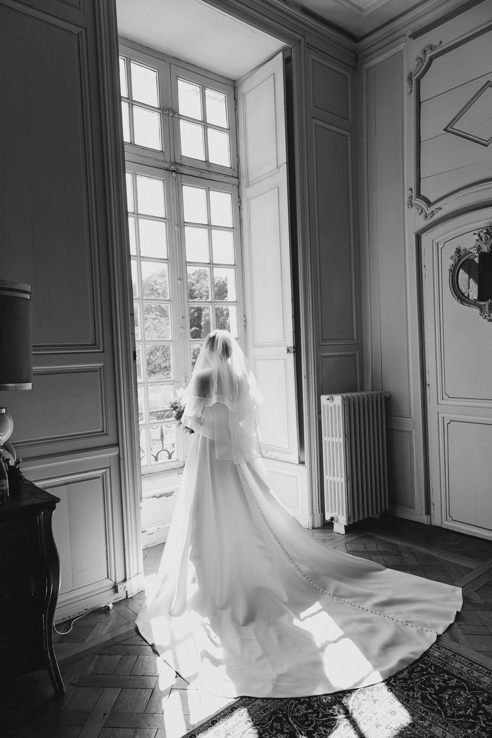 Black and white photograph of a flowing wedding dress silhouetted against bright windows.