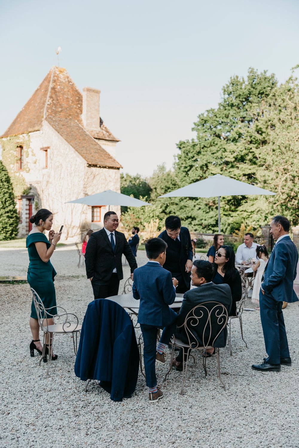 Wedding guests gather in a courtyard with metal chairs in front of a charming French countryside chateau.