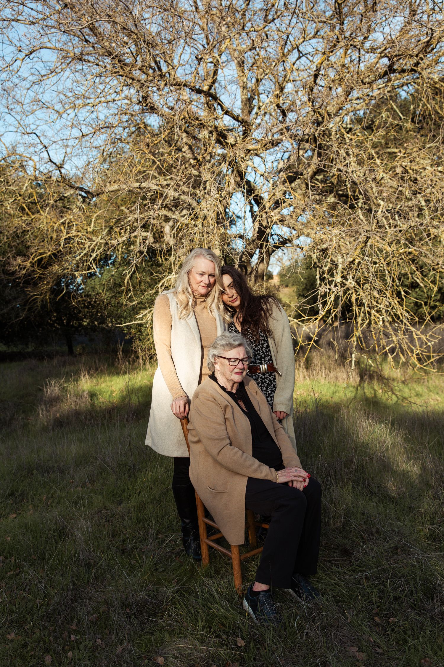 Intimate outdoor portrait session in a grassy field with soft golden light filtering through bare tree branches.