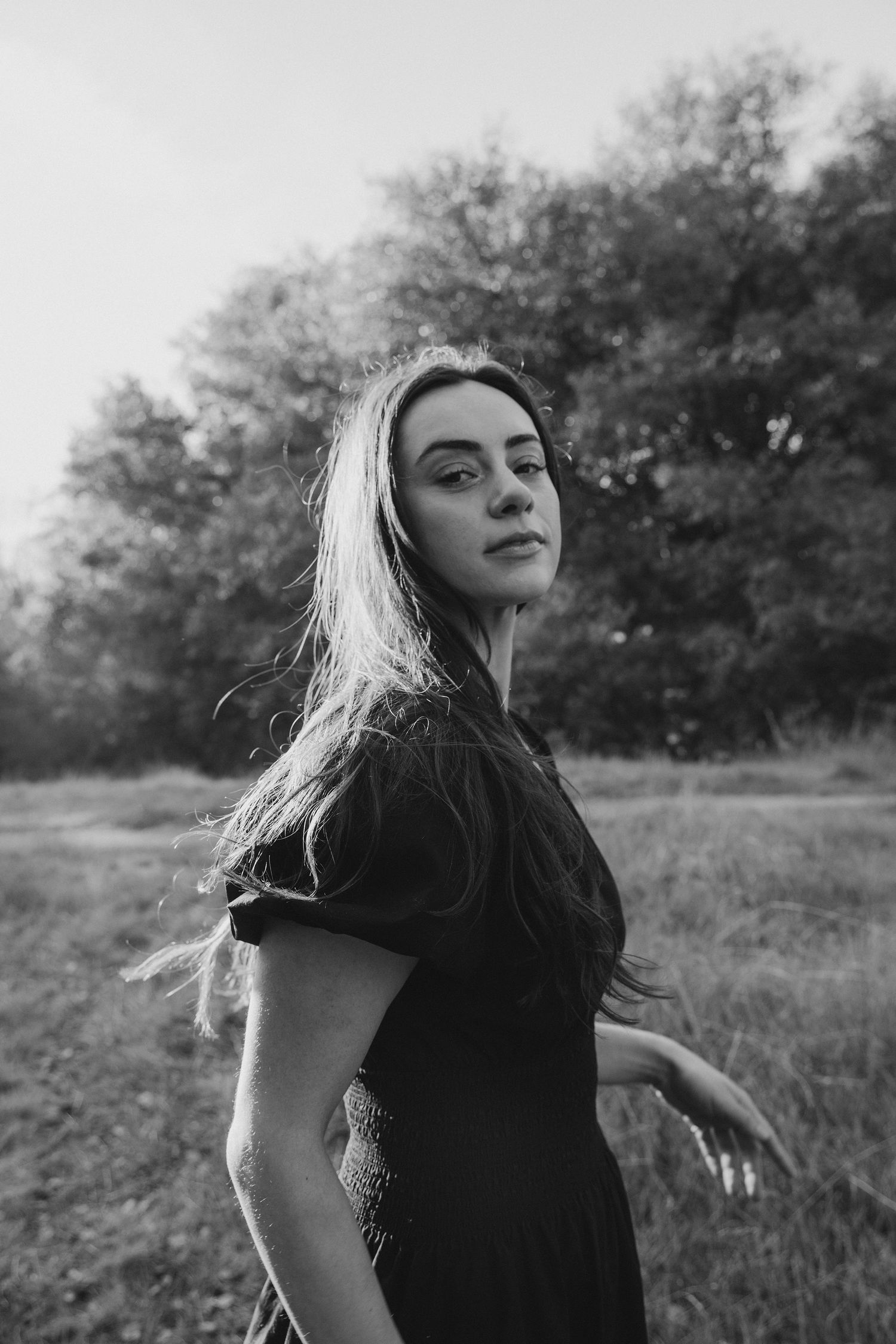 Black and white portrait with dramatic lighting and windswept hair against a natural backdrop.