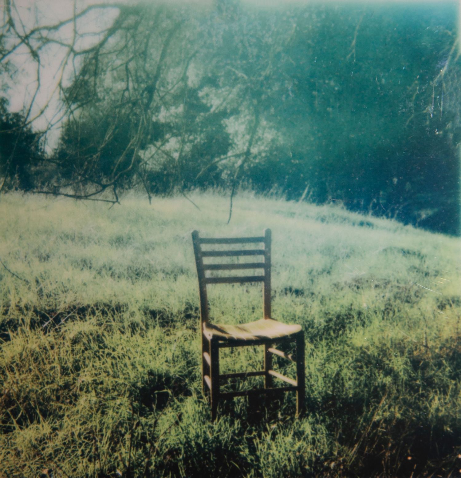 Vintage teal-tinted photograph of empty wooden chairs in misty field.