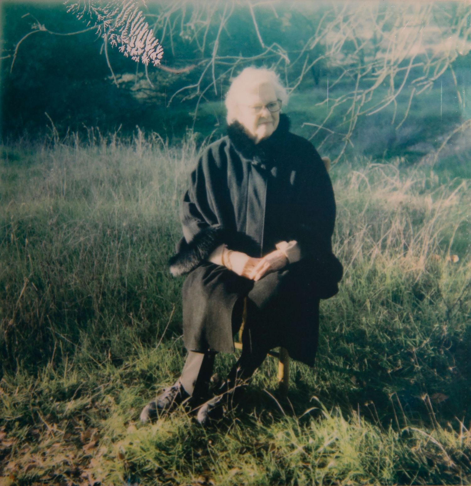 Teal-toned nostalgic photograph showing figure seated in grassy field.