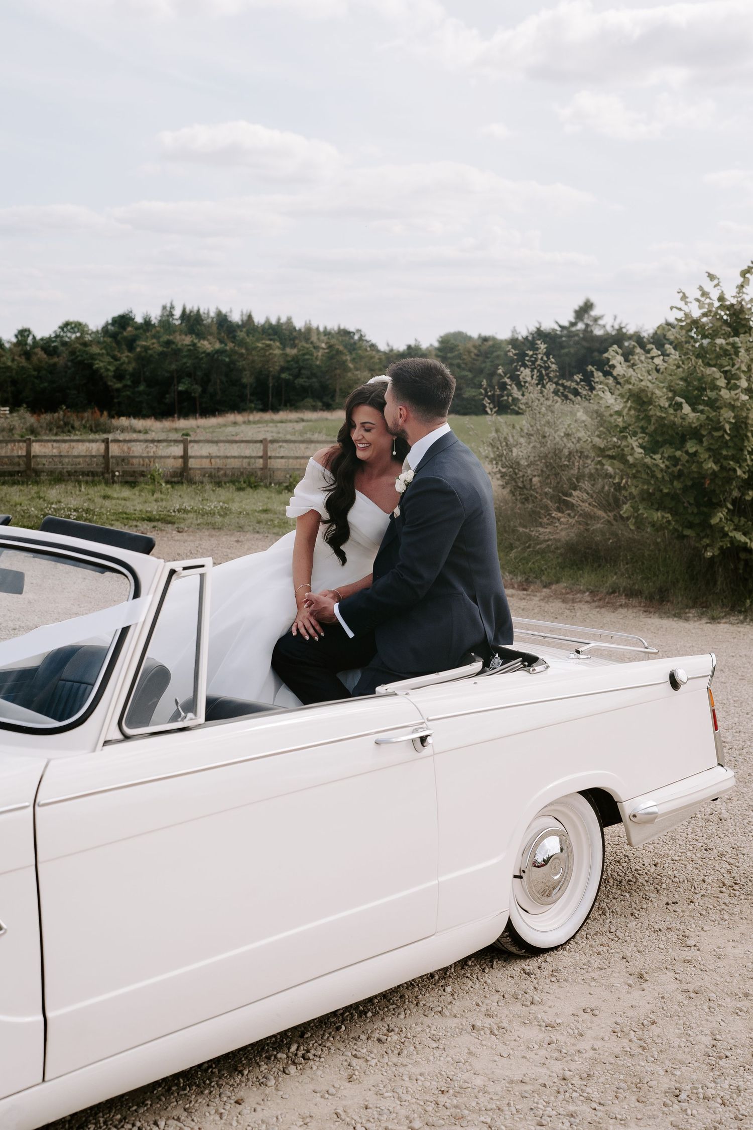 groom kissing bride while sat on backseat of vintage car at yardspace old gore in cirencester