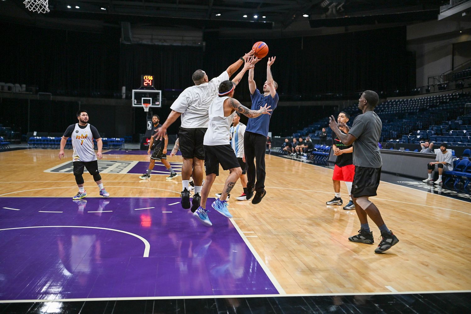 Players engage in an intense basketball scrimmage on a purple indoor court.