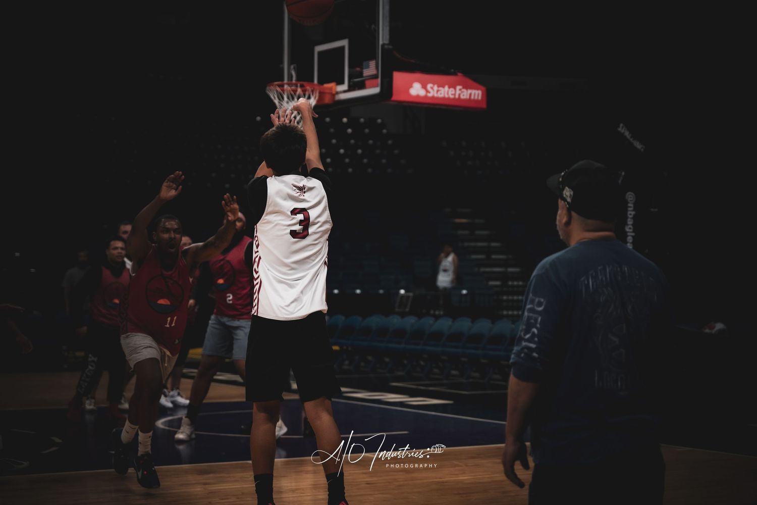 Basketball player wearing number 3 jersey shoots at the hoop during a game in a dark arena with State Farm signage.