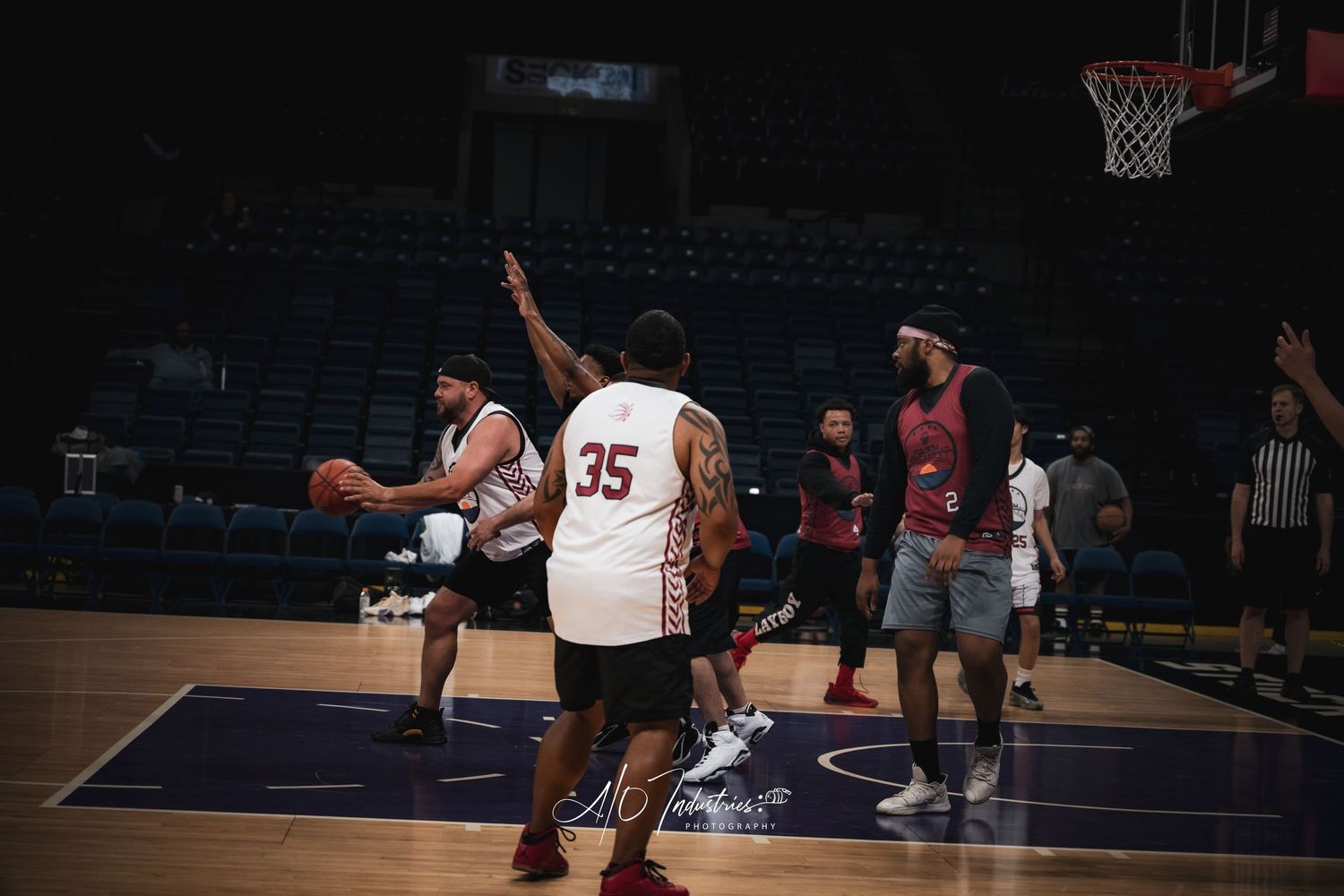 Basketball players compete indoors on a hardwood court with empty arena seats and a hoop visible in the background.