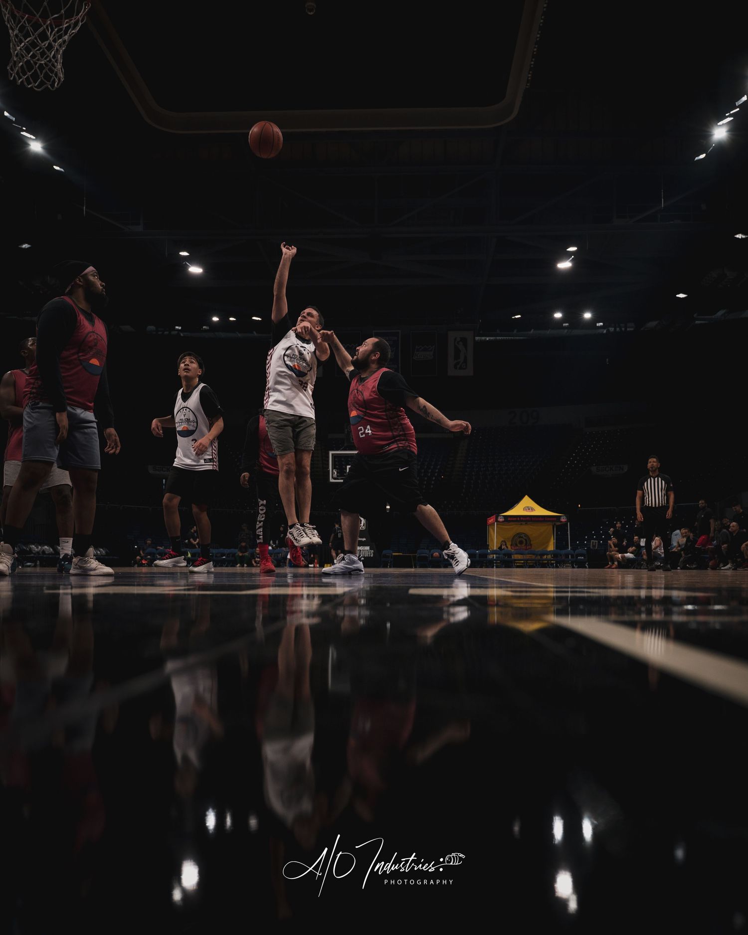 Players compete in an indoor basketball game under bright arena lights, with one player shooting over a defender.