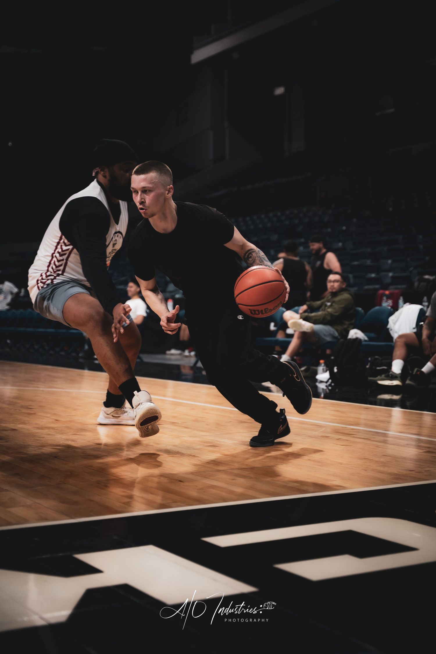 A basketball player in a black shirt dribbles past a defender during an indoor arena game.