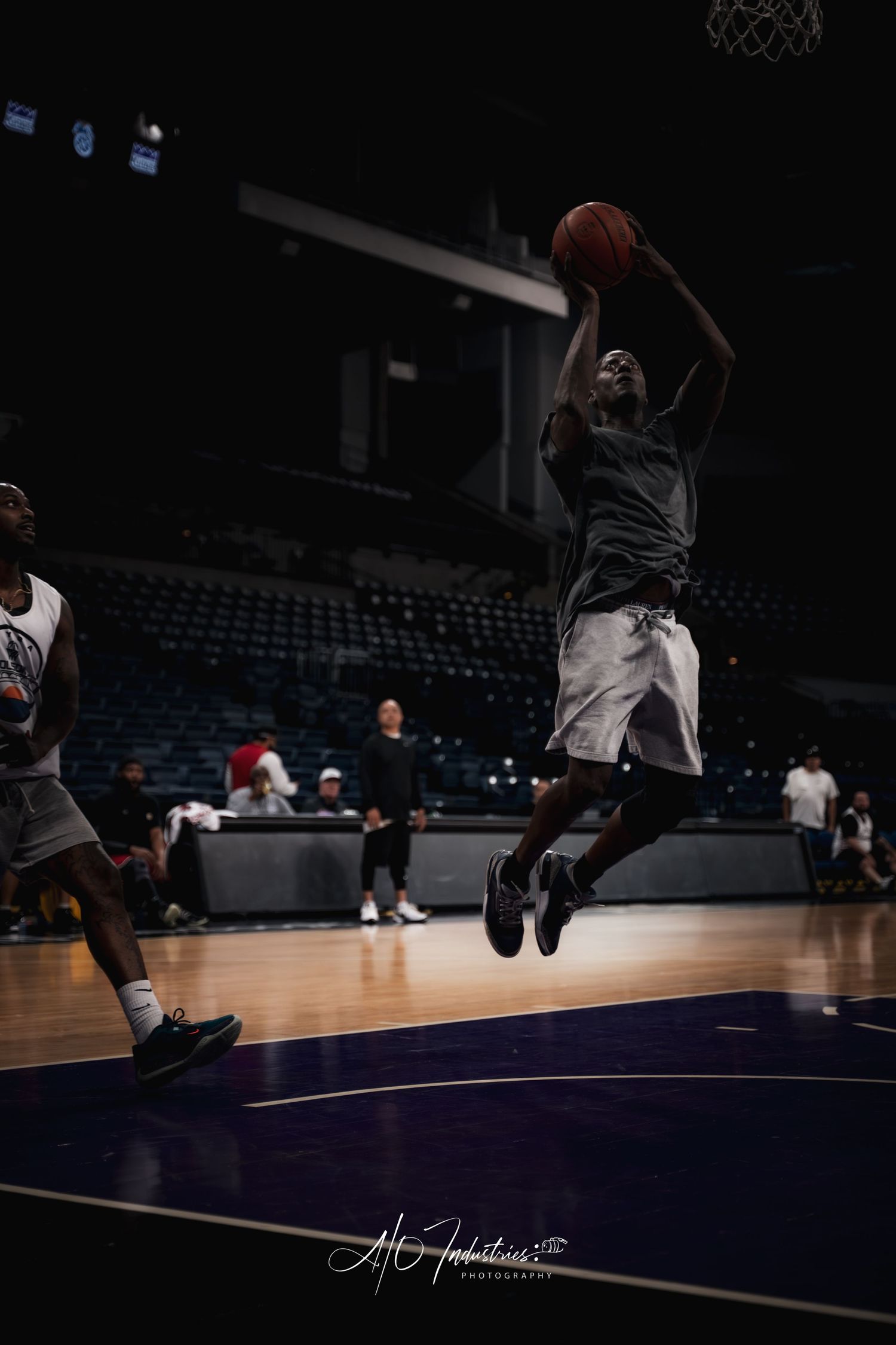 Athletic basketball player leaps for a layup shot in a dark indoor arena during practice.