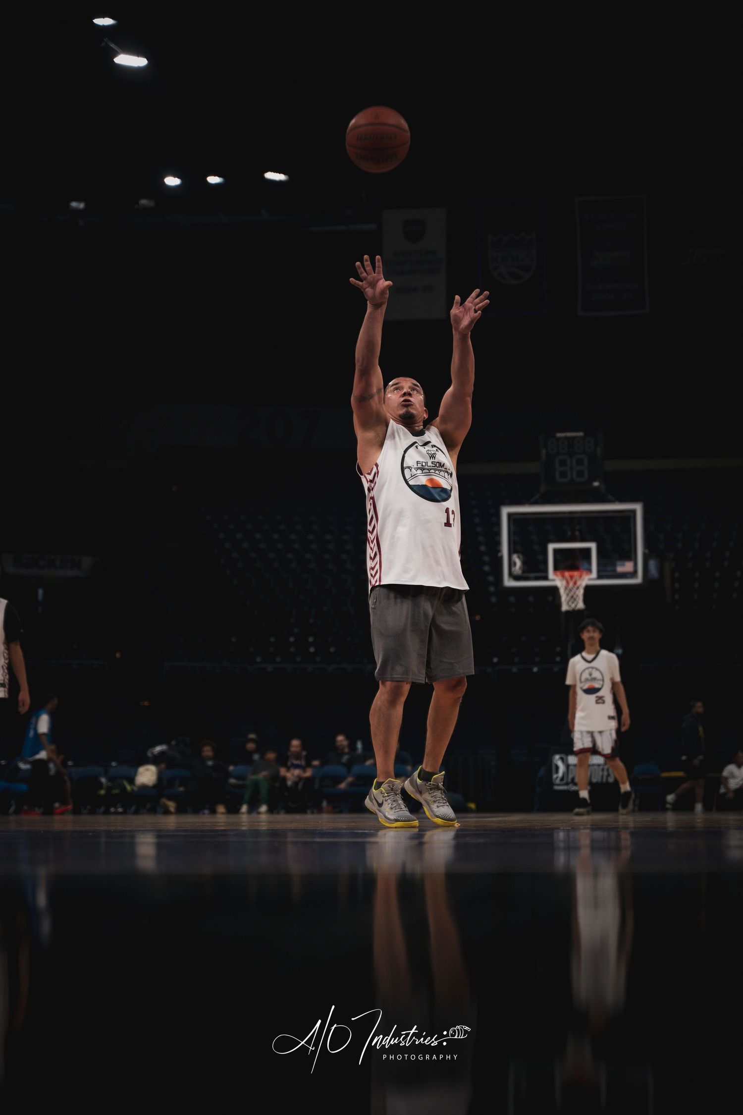 A basketball player shoots a jump shot in a dark indoor arena during a game.