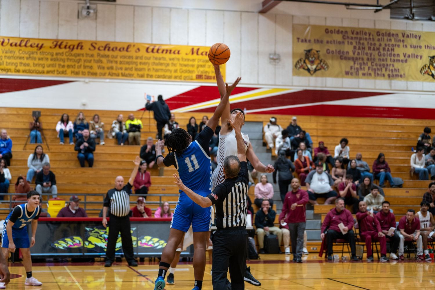 A basketball game in progress in a high school gymnasium with teams in blue and white uniforms.