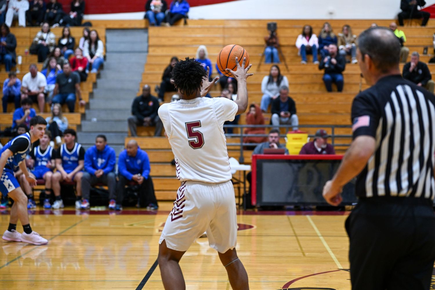 High school basketball players compete in a gymnasium with spectators watching from bleachers.