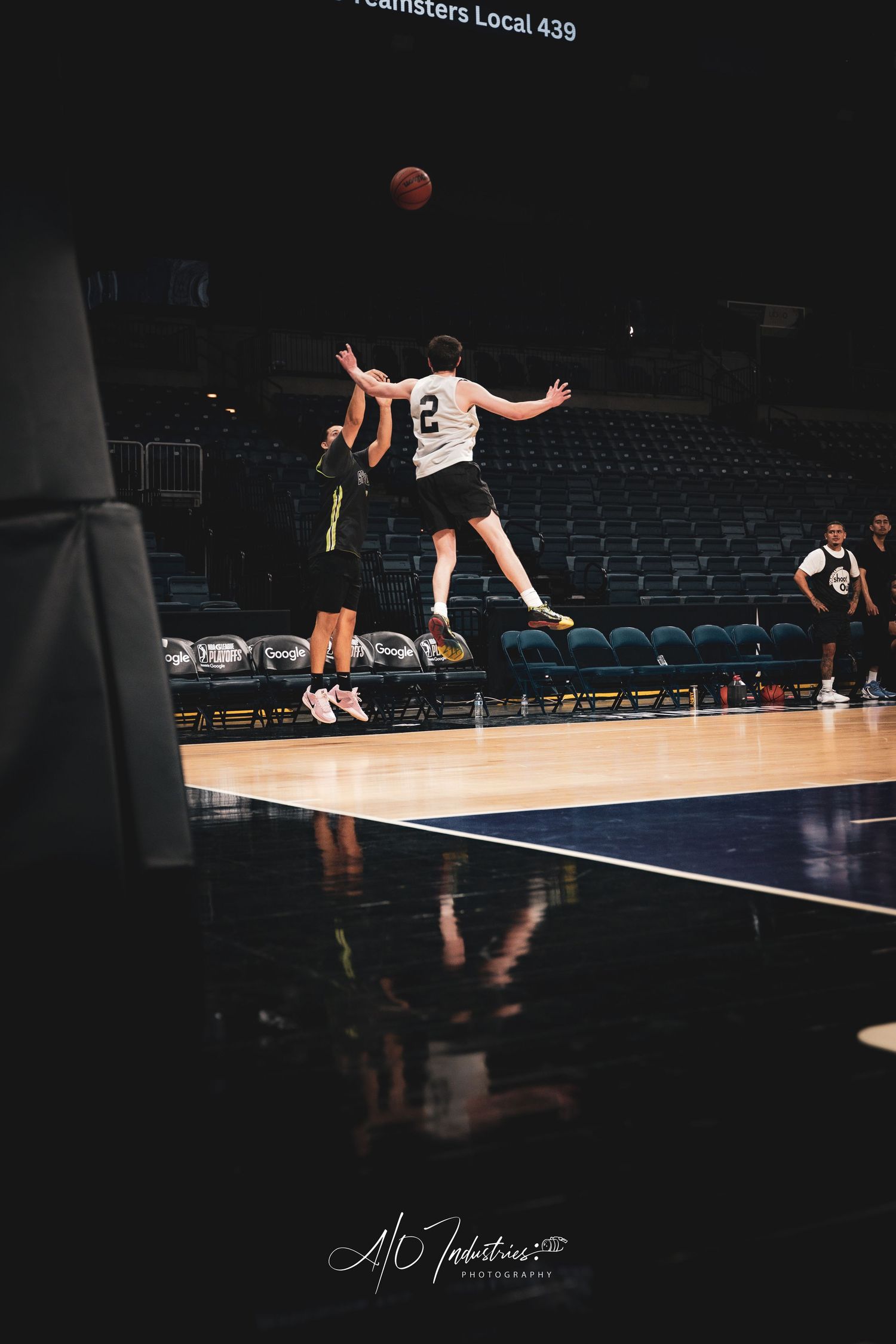 Two basketball players jump for the ball near the court boundary during an indoor arena practice session.
