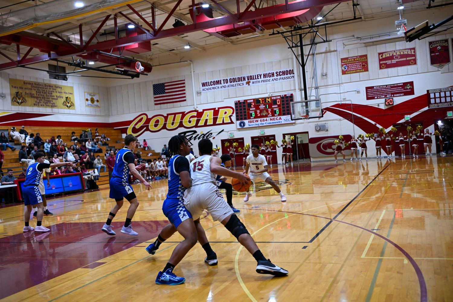 Players in blue and white uniforms compete during a basketball game in a school gymnasium.