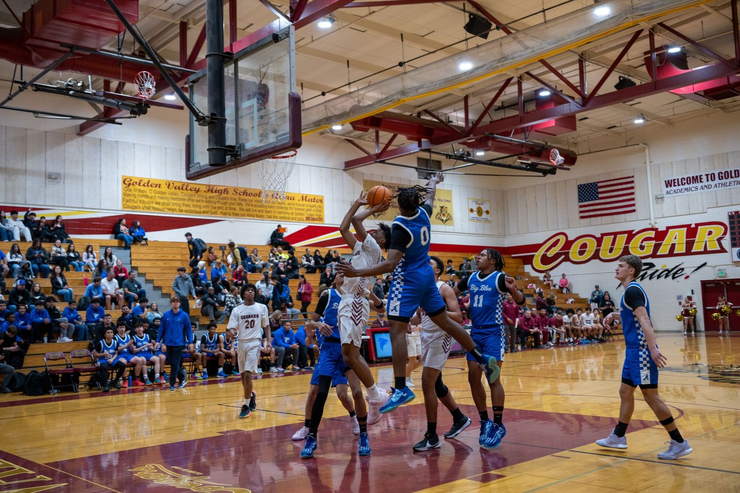 Basketball players compete on the court during a high school game with spectators watching.