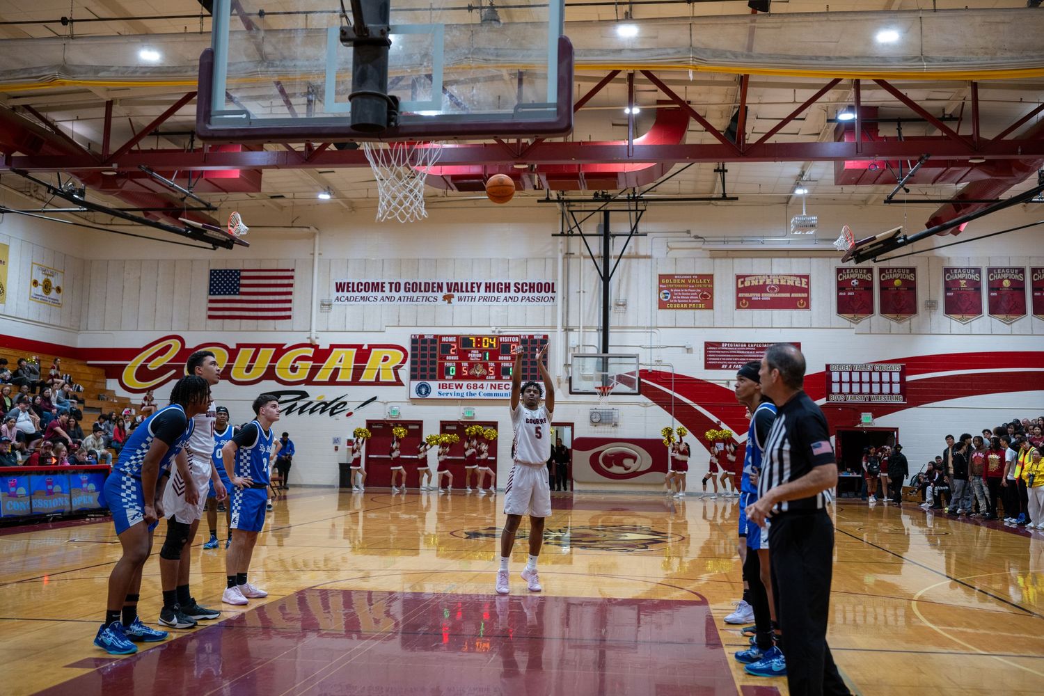 Wide view of a high school basketball game showing players and spectators in the gymnasium.