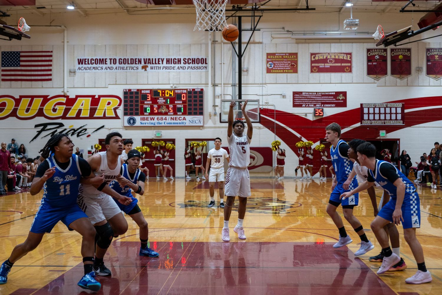 Basketball teams face off under the Cougar mascot banner during a competitive high school game.