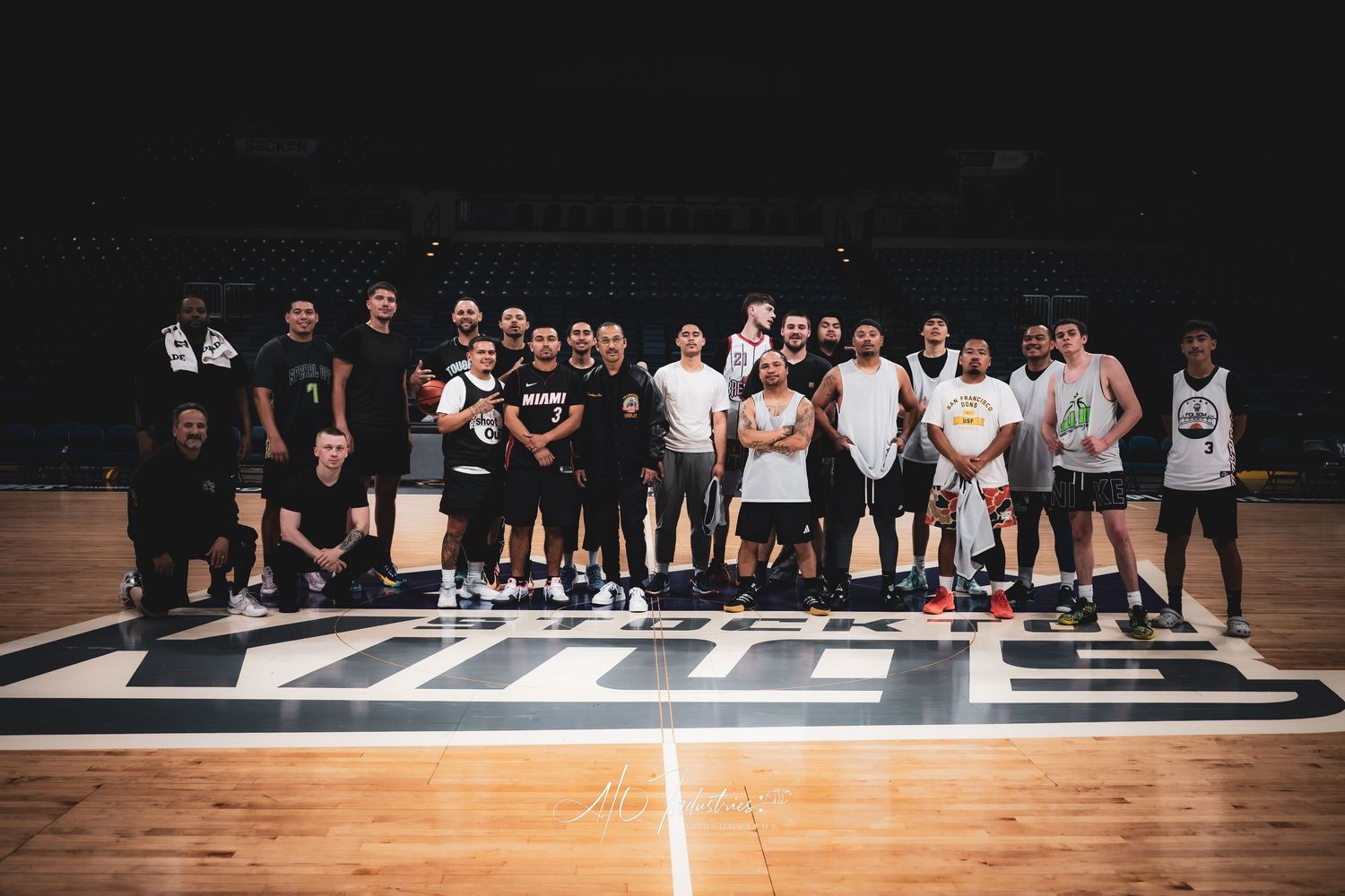 Large group of basketball players pose together for team photo on indoor arena court center logo.