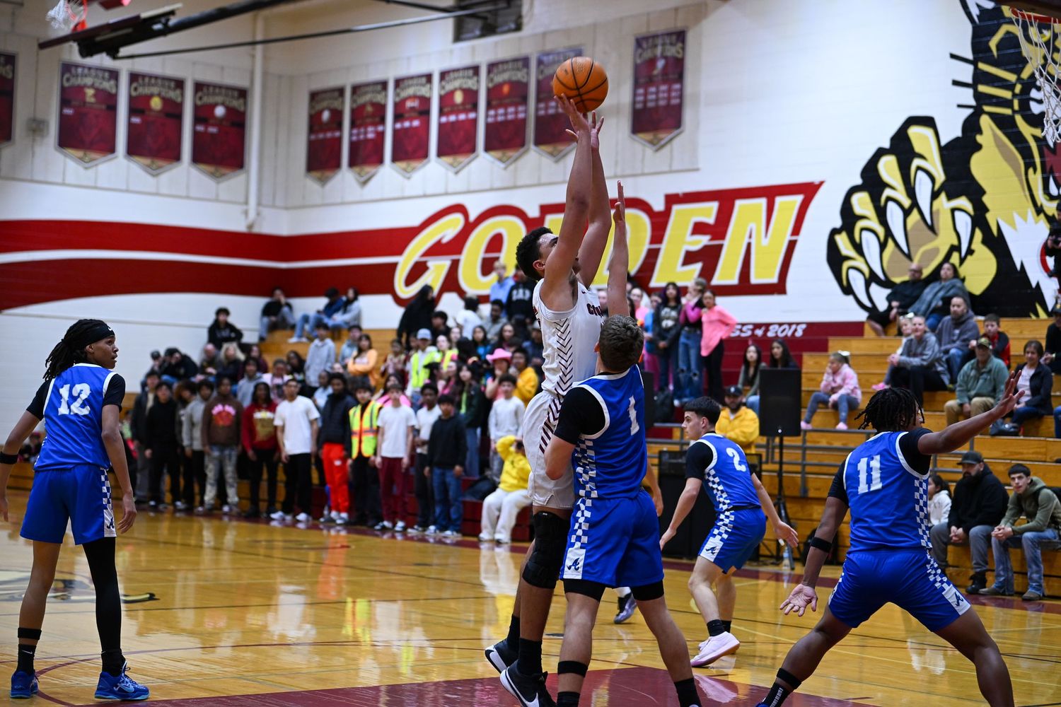 High school basketball players compete for a rebound during an intense game in a gymnasium.