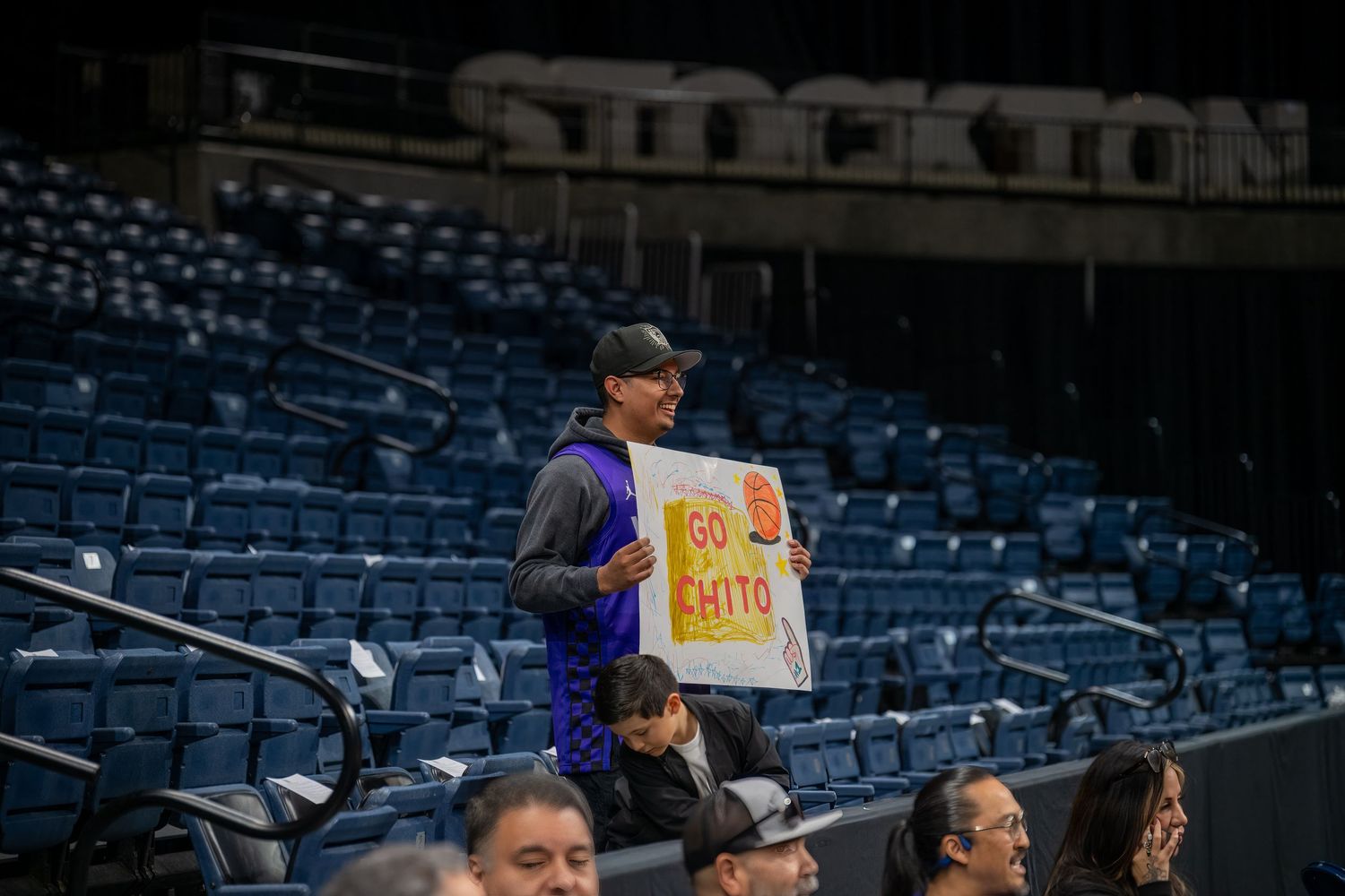 Fan holds up a sign in empty stadium seats during a basketball game.
