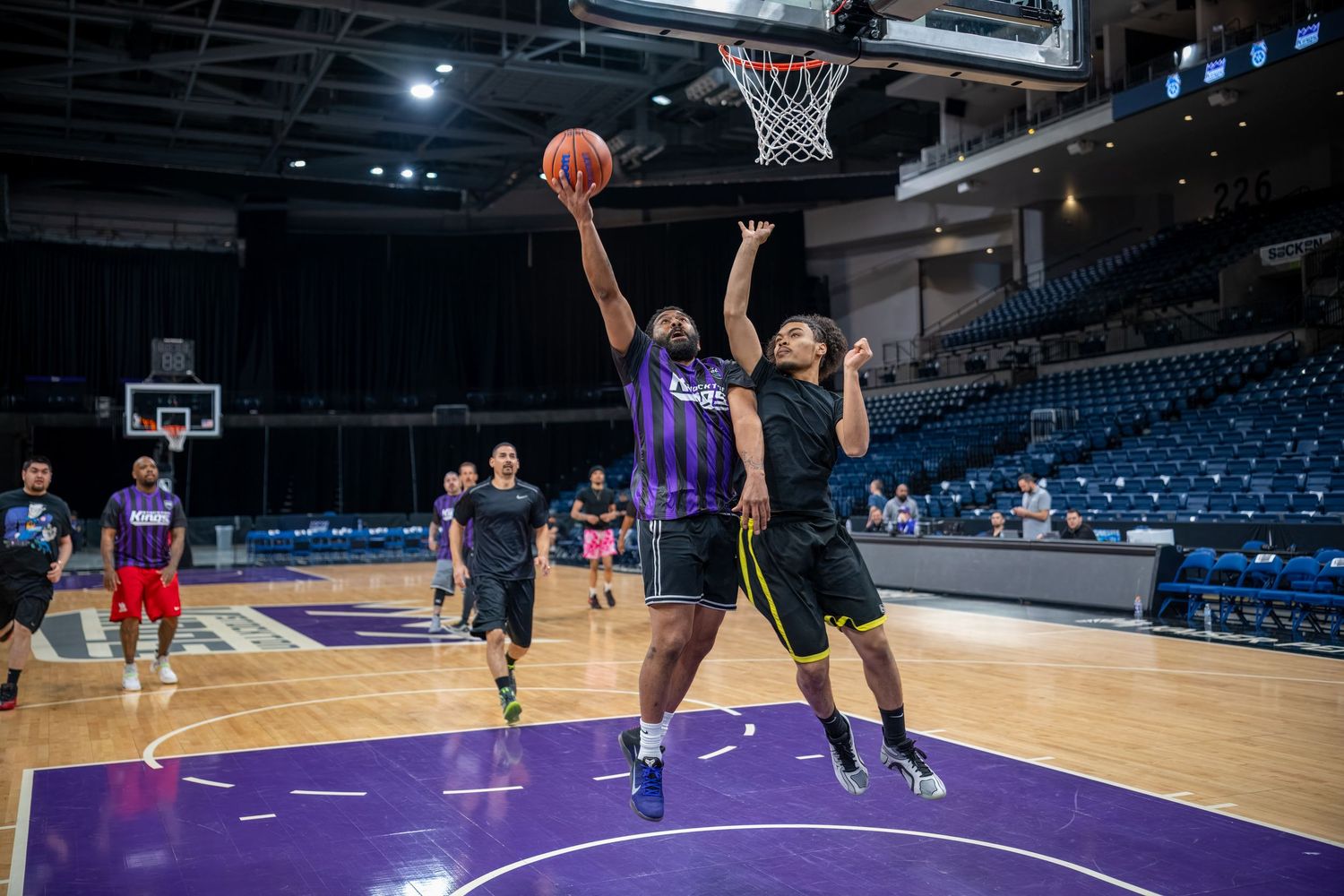 Basketball players practice layups on a purple court during a training session.